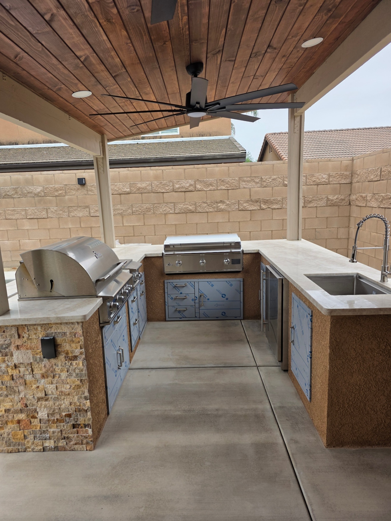 Custom covered outdoor kitchen with dual stainless grills, stone base, and tongue-and-groove wood ceiling